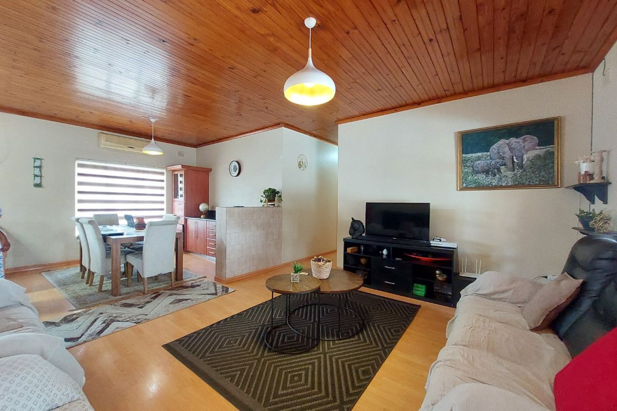 Open-plan living and dining area featuring warm timber ceilings, laminate flooring, and a tiled partition wall separating the kitchen space.