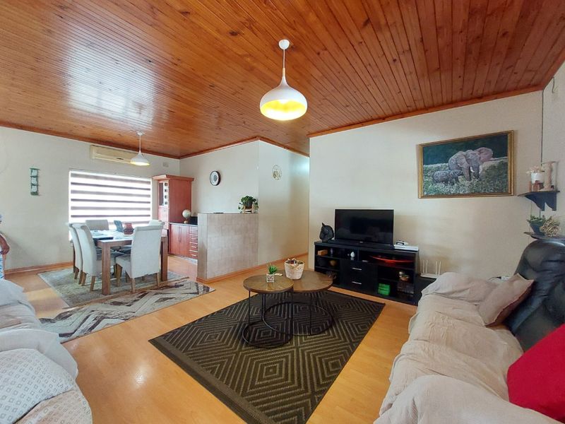 Open-plan living and dining area featuring warm timber ceilings, laminate flooring, and a tiled partition wall separating the kitchen space.