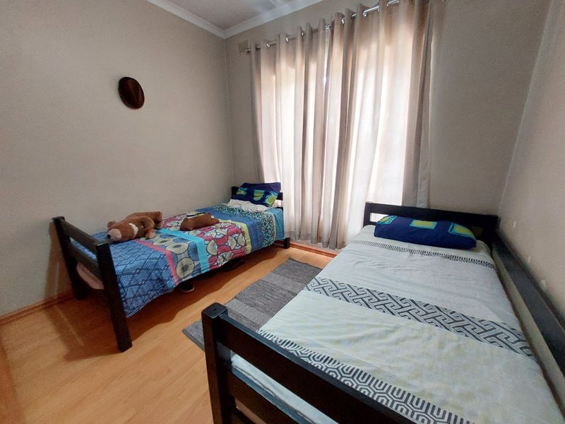A functional bedroom featuring laminate flooring, neutral wall tones, and large windows with curtain rails, providing a comfortable space for rest.