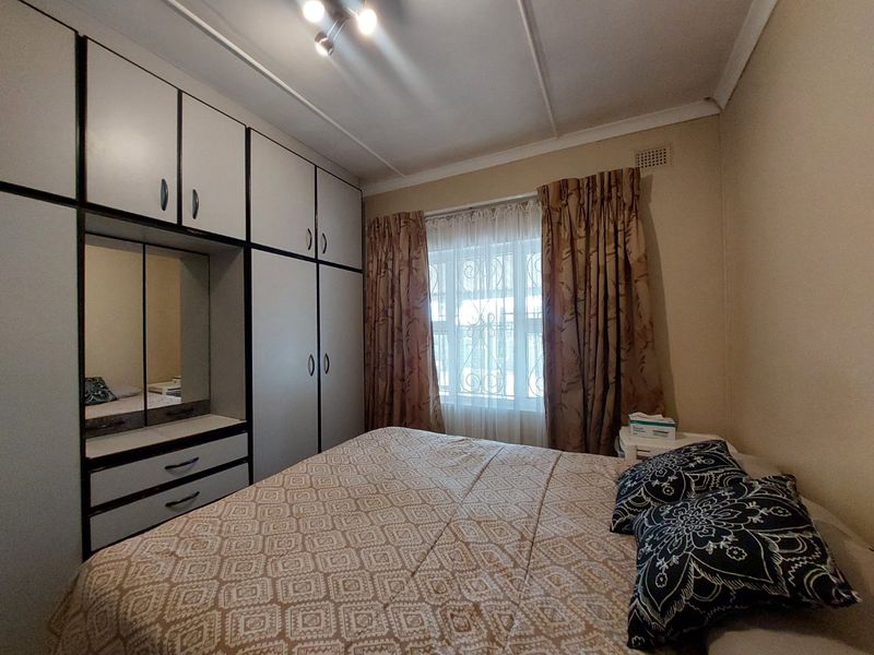 A bedroom featuring built-in cupboards with integrated vanity mirror, neutral wall finishes, and a window fitted with security bars.