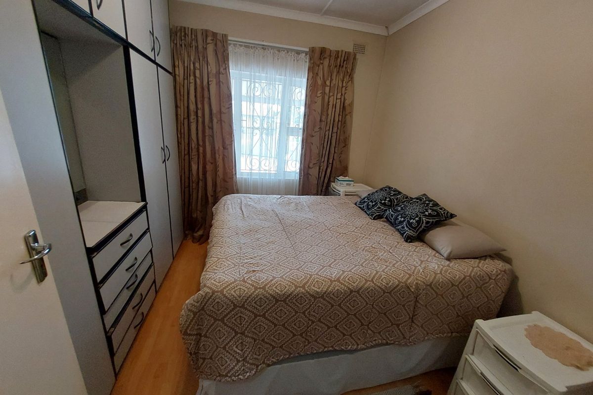 A functional bedroom featuring built-in cupboards, laminate flooring, and a window fitted with security bars.