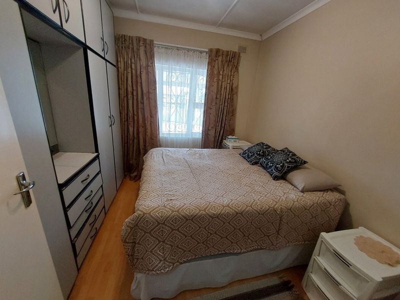 A functional bedroom featuring built-in cupboards, laminate flooring, and a window fitted with security bars.