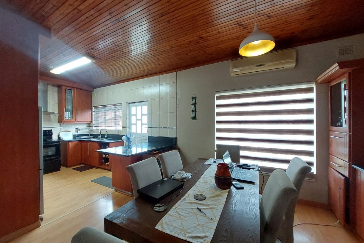 Open-plan kitchen and dining area featuring timber ceilings, granite countertops, built-in cabinetry, and laminate flooring, creating a functional and connected living space.