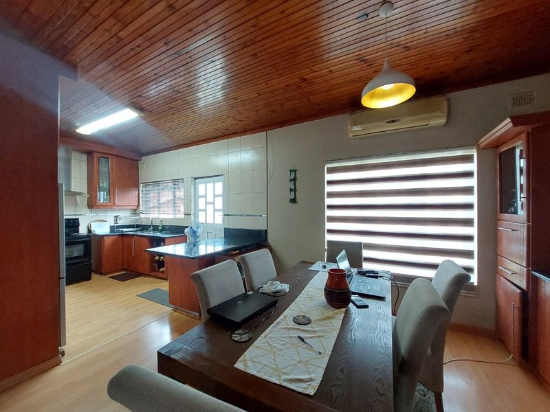 Open-plan kitchen and dining area featuring timber ceilings, granite countertops, built-in cabinetry, and laminate flooring, creating a functional and connected living space.