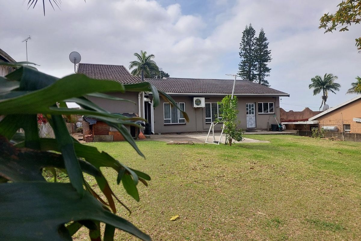 Rear view of the house featuring a tiled roof, concrete patio area, and a spacious garden with boundary walling.