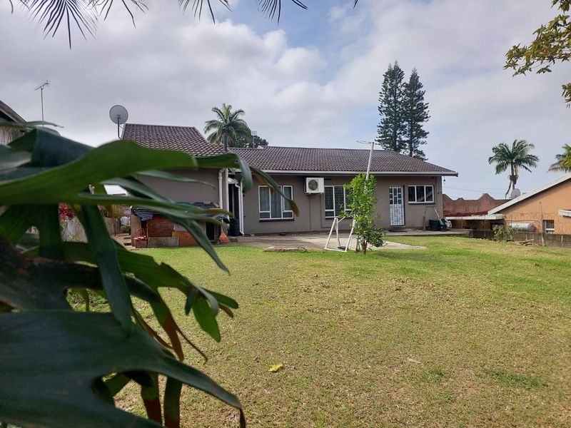 Rear view of the house featuring a tiled roof, concrete patio area, and a spacious garden with boundary walling.