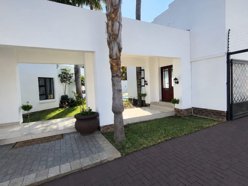 Modern front facade featuring a paved driveway, covered entrance walkway, and secure perimeter fencing with a gated entry.