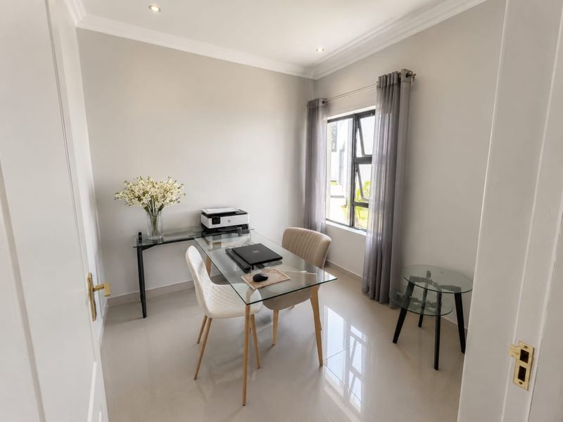 A bright and modern home office featuring neutral walls, tiled flooring, recessed lighting, and a large window allowing for natural light.