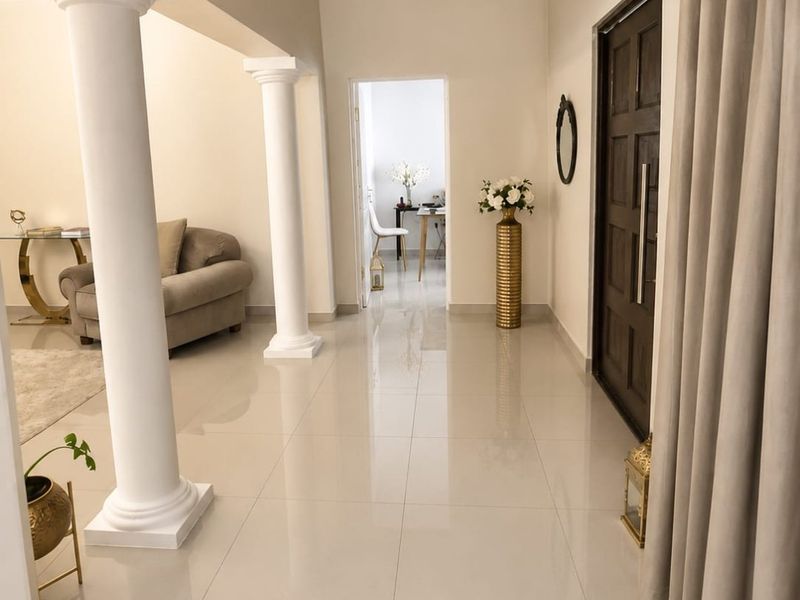 A bright and welcoming entrance hall featuring polished porcelain floor tiles, decorative columns, and a solid wood front door.