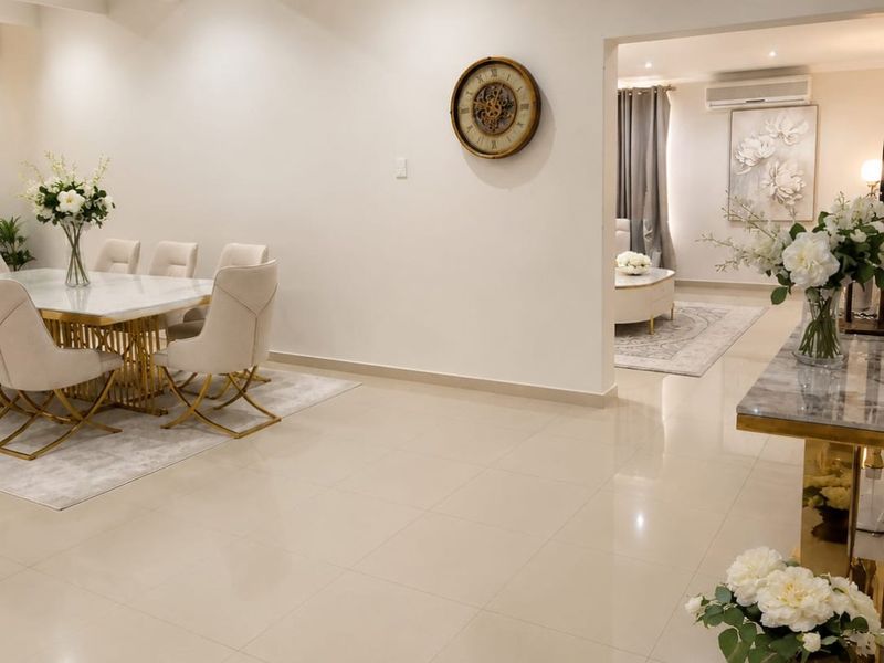 Spacious open-plan living and dining area featuring high ceilings with exposed beams, polished porcelain floor tiles, and modern recessed lighting.