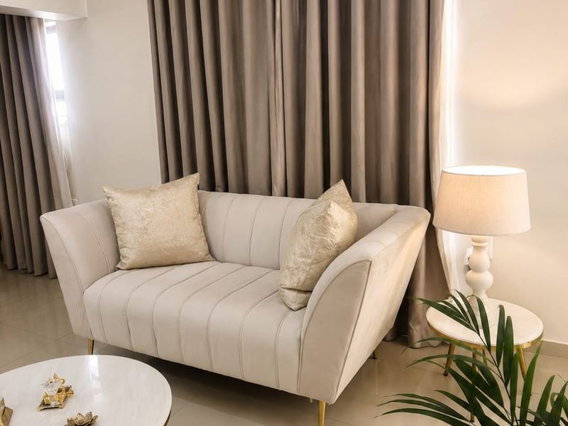 A well-maintained living room area featuring neutral tiled flooring and floor-to-ceiling curtain treatments.