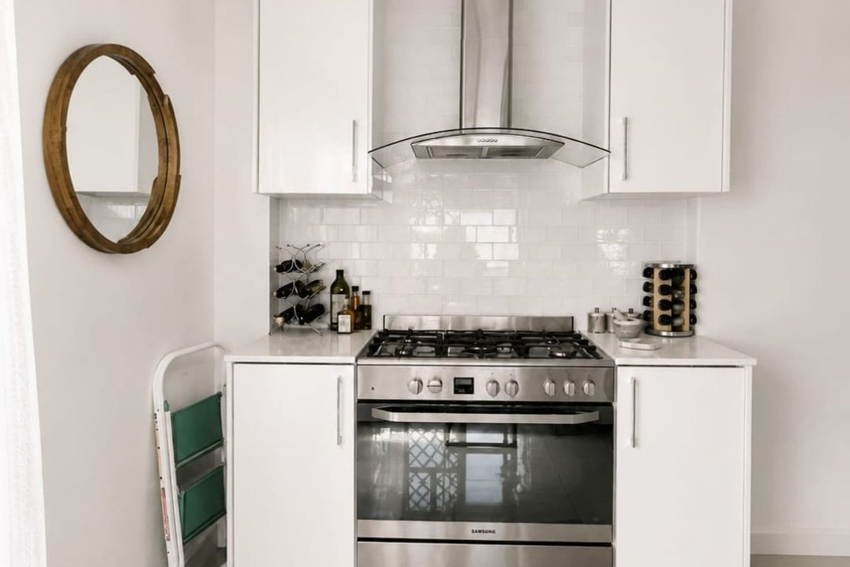 A clean, modern kitchen featuring white cabinetry, a stainless steel gas stove with extractor fan, and a classic subway tile backsplash.