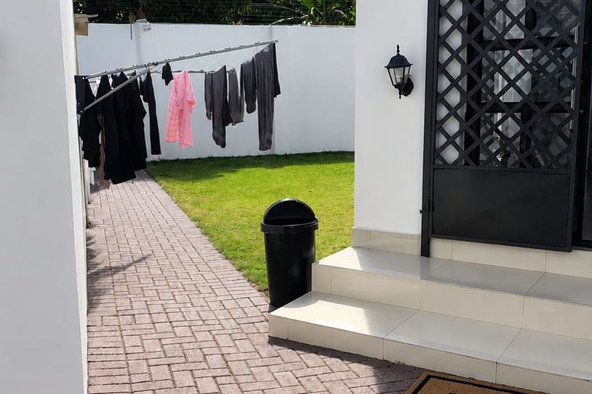 A well-maintained rear exterior area featuring a paved walkway, tiled steps leading to a security gate, and a private lawn enclosed by boundary walls.