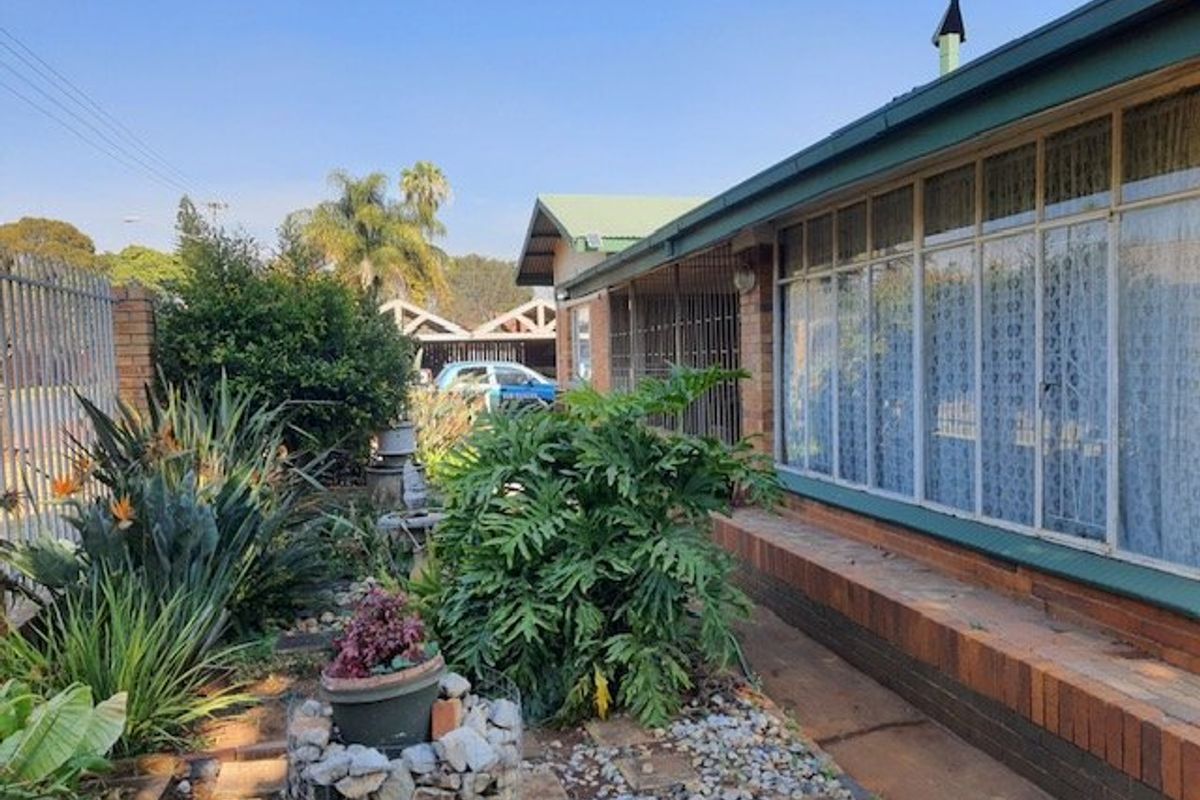 Rear exterior view of the house featuring a brick facade, metal window frames with security bars, and a landscaped garden area.