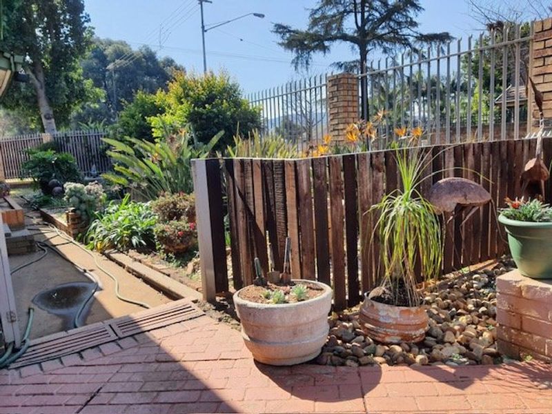 A residential garden area featuring brick paving, timber slat fencing, and established landscaping with a metal security perimeter fence.
