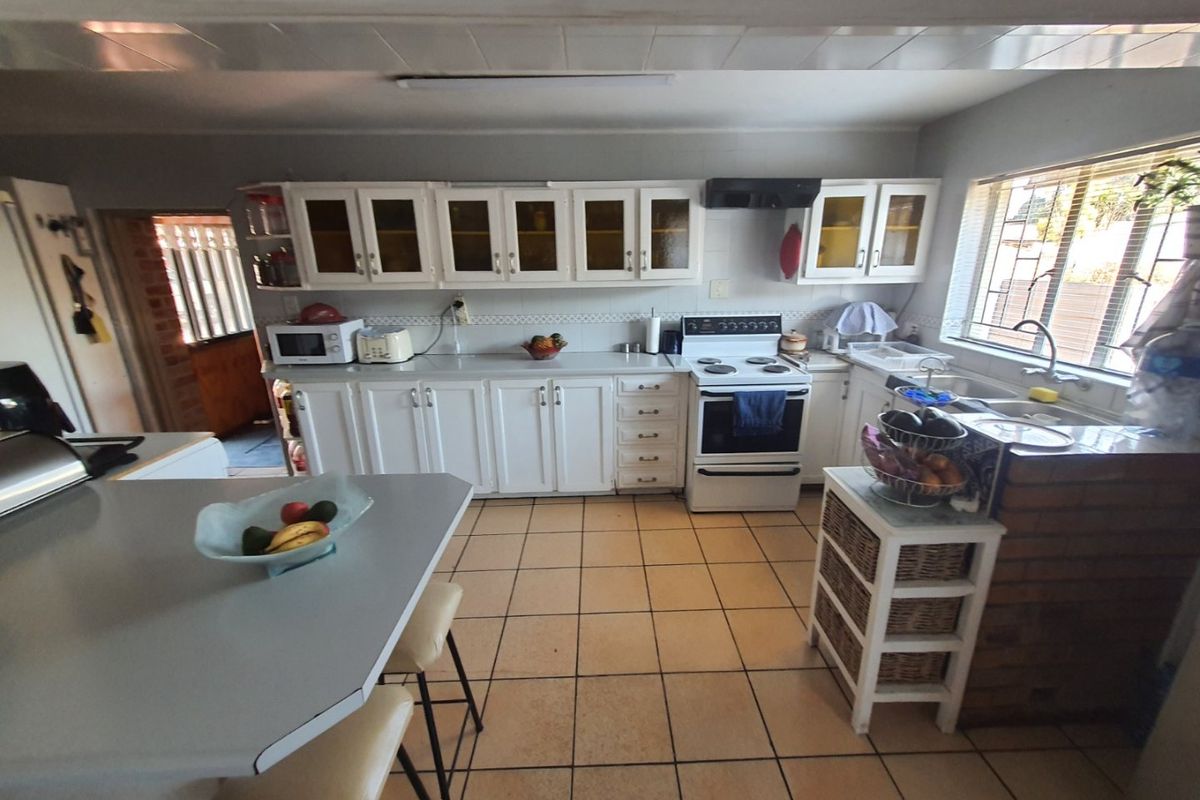 A functional kitchen featuring white cabinetry, a freestanding stove with extractor fan, tiled flooring, and a breakfast counter area.