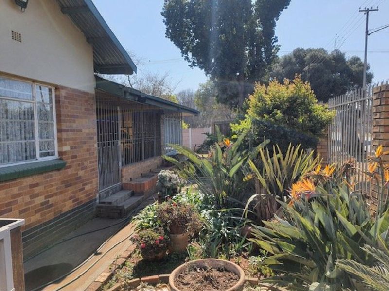 Front exterior view of a brick house featuring security bars on windows, a corrugated metal roof, and a landscaped garden area.