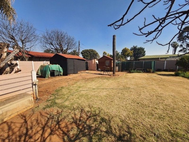 A spacious rear garden area featuring a lawn, perimeter precast concrete walling, and multiple storage sheds.