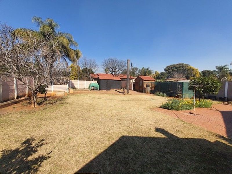 Spacious rear garden featuring a large lawn area, brick paved patio section, and multiple utility sheds enclosed by perimeter walling.