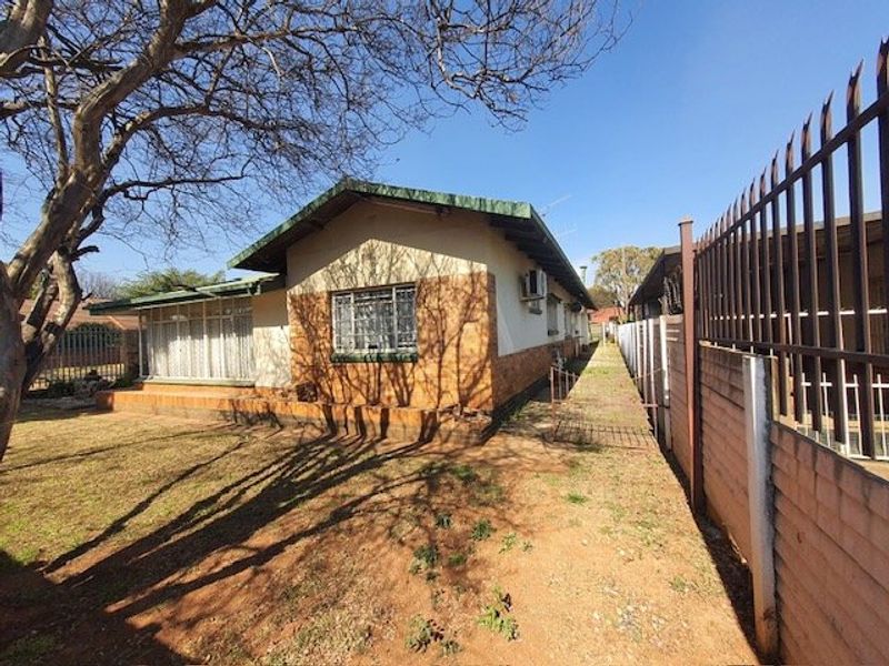 Rear view of a single-story brick house featuring security bars, an external air conditioning unit, and a fenced perimeter.