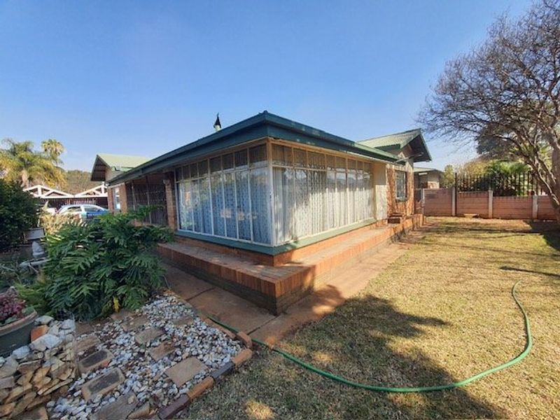 Rear view of the property featuring a brick facade, an enclosed sunroom with large windows, and a surrounding garden area.