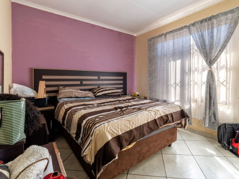 A bedroom featuring tiled flooring, a built-in headboard, and a security gate on the window. The room requires cosmetic updates to the wall finishes.
