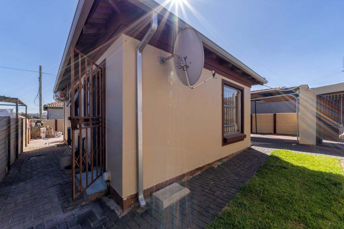 Rear exterior view of the property featuring paved walkways, a secure gate, and a satellite dish installation.