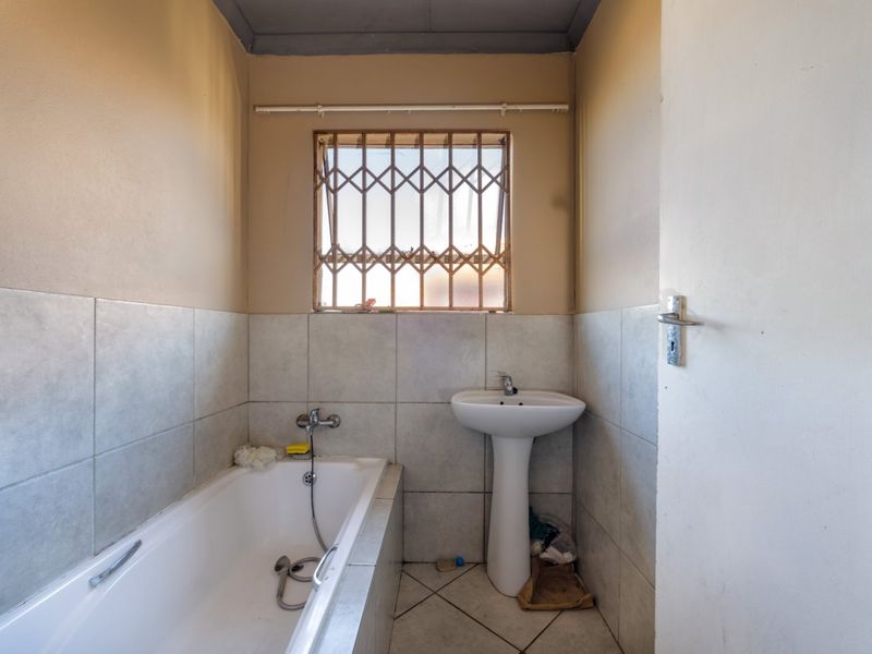 A functional bathroom featuring a pedestal basin, built-in bathtub, and tiled finishes, requiring minor cosmetic updates to enhance its appeal.