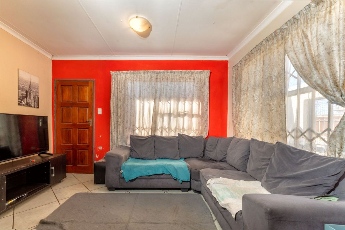 A living room featuring tiled flooring, a timber door with security gate, and a bold red accent wall, requiring minor cosmetic updates.