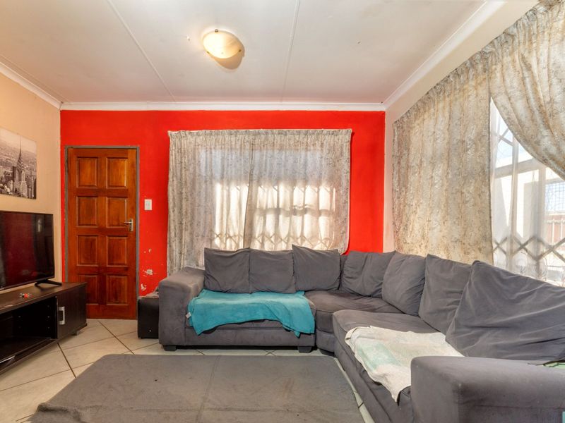 A living room featuring tiled flooring, a timber door with security gate, and a bold red accent wall, requiring minor cosmetic updates.