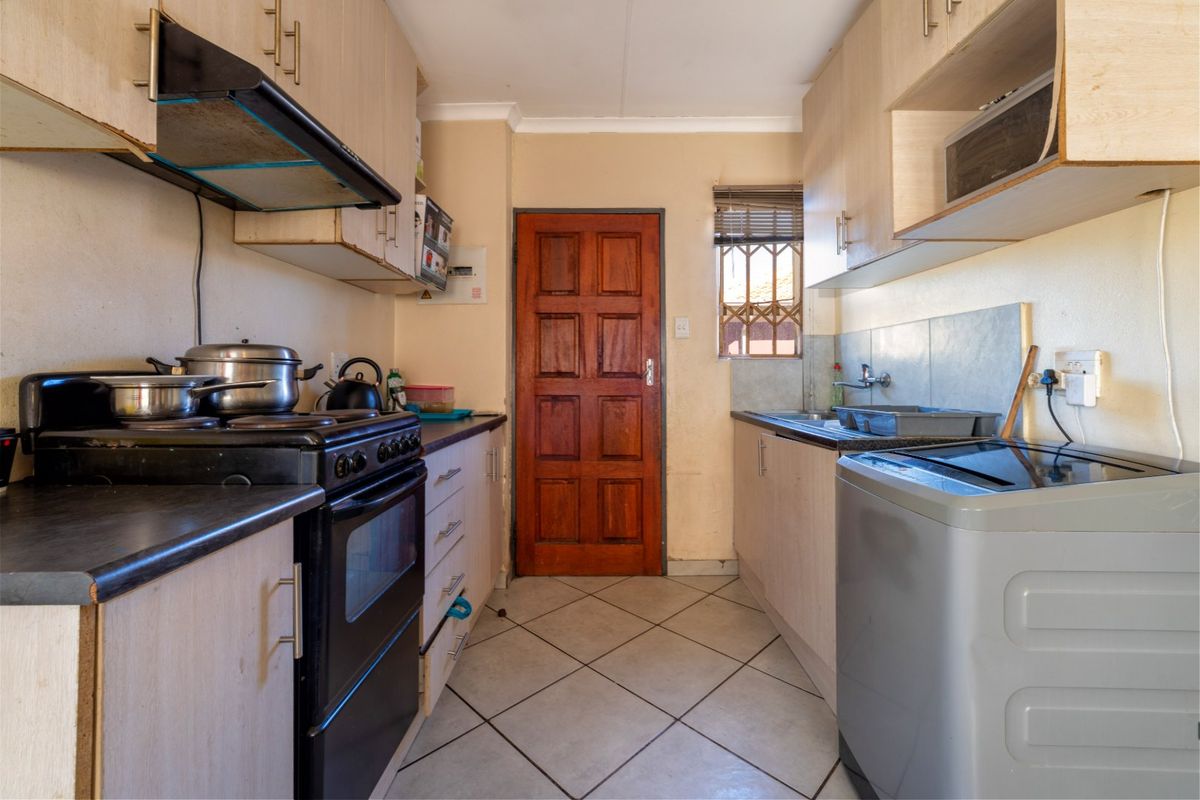 A compact kitchen featuring built-in cabinetry, a freestanding stove with extractor fan, and tiled flooring, offering a functional layout in need of cosmetic updates.