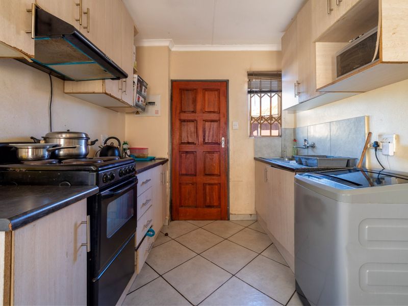 A compact kitchen featuring built-in cabinetry, a freestanding stove with extractor fan, and tiled flooring, offering a functional layout in need of cosmetic updates.