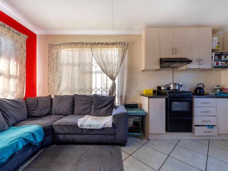 Open-plan living area featuring a compact kitchen with built-in cabinetry, a freestanding stove, and tiled flooring throughout.