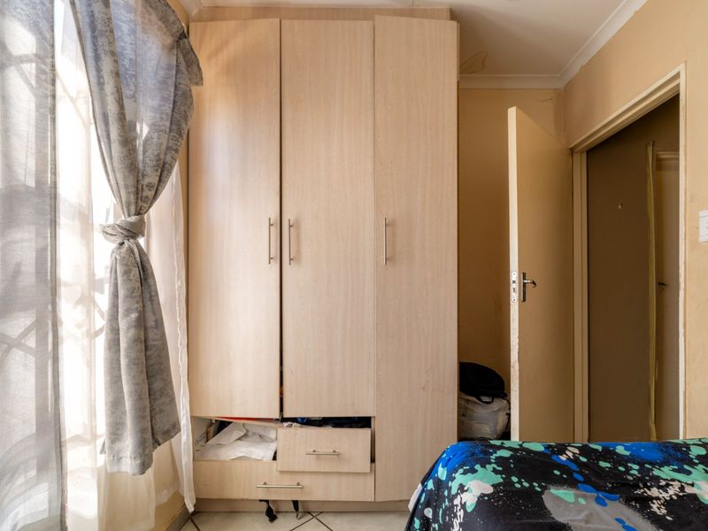 A bedroom featuring a light wood-finish built-in wardrobe with integrated drawers and tiled flooring.