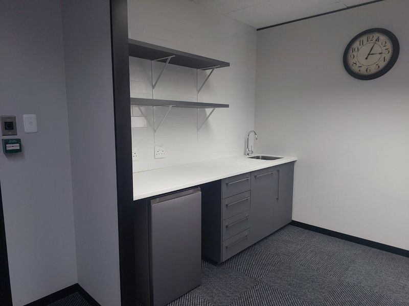 A clean, modern kitchenette area featuring built-in grey cabinetry, a stainless steel sink, and wall-mounted shelving, suitable for office or commercial use.