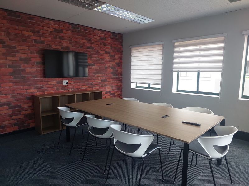 A modern, well-maintained office meeting room featuring an exposed brick accent wall, recessed ceiling lighting, and neutral carpet tiles.