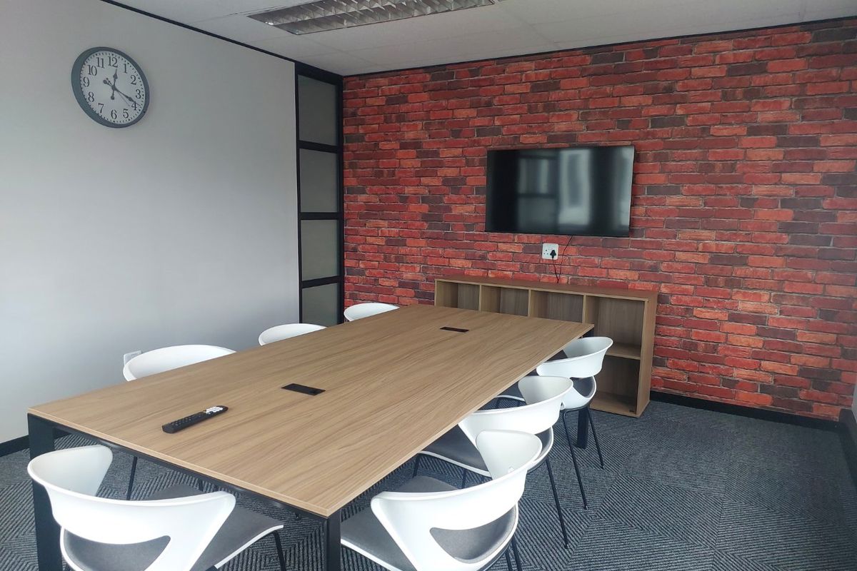 A modern commercial office meeting room featuring a brick-style accent wall, suspended ceiling, and professional carpet tile flooring.