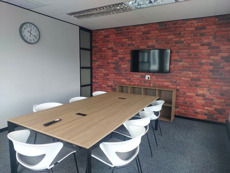 A modern commercial office meeting room featuring a brick-style accent wall, suspended ceiling, and professional carpet tile flooring.