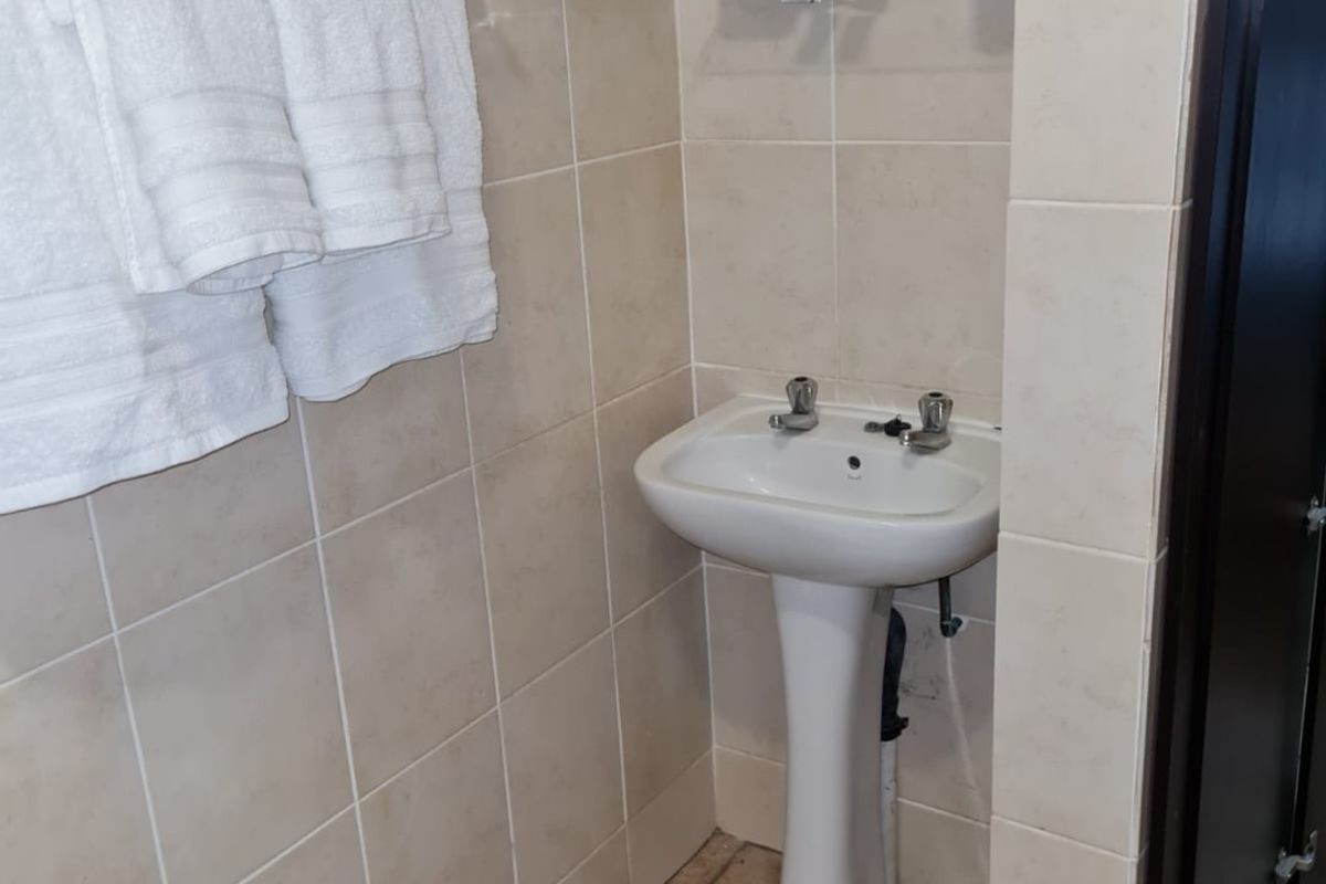A compact bathroom featuring a pedestal basin, tiled walls with a mosaic accent, and a functional towel rail.