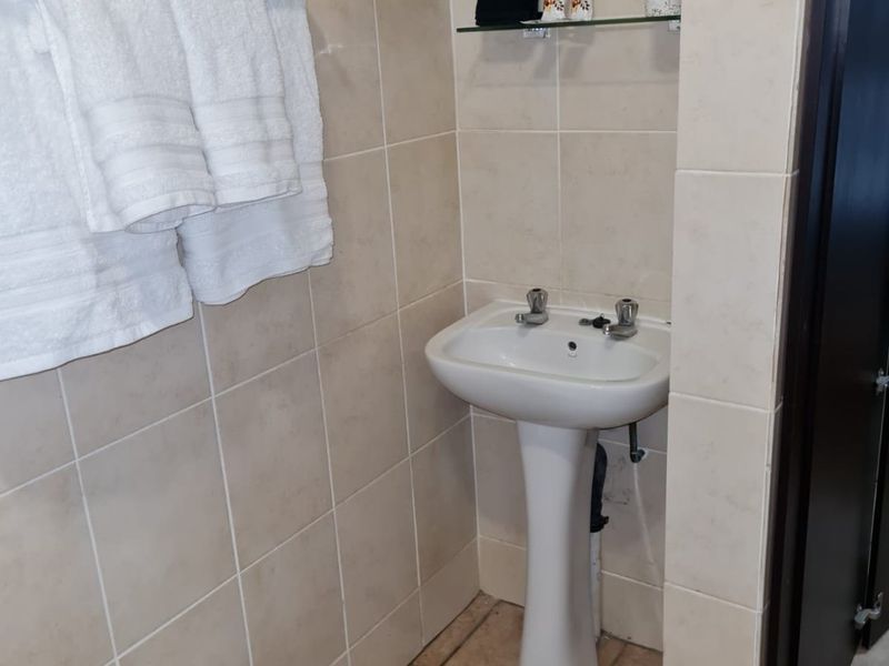 A compact bathroom featuring a pedestal basin, tiled walls with a mosaic accent, and a functional towel rail.