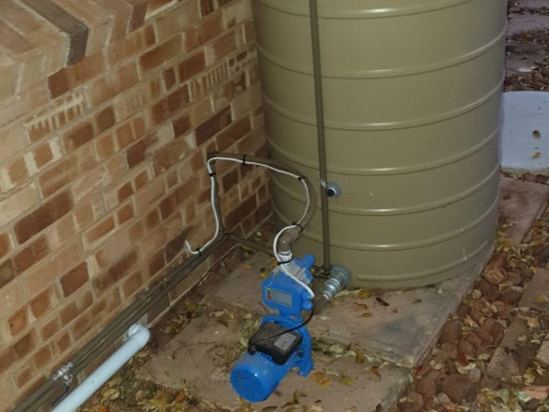 Exterior view showing a slimline water tank and pump system installed against the brick wall of the townhouse.