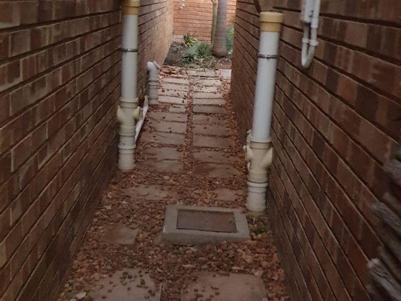 A narrow side passage between brick walls featuring paved stepping stones and exposed drainage infrastructure.