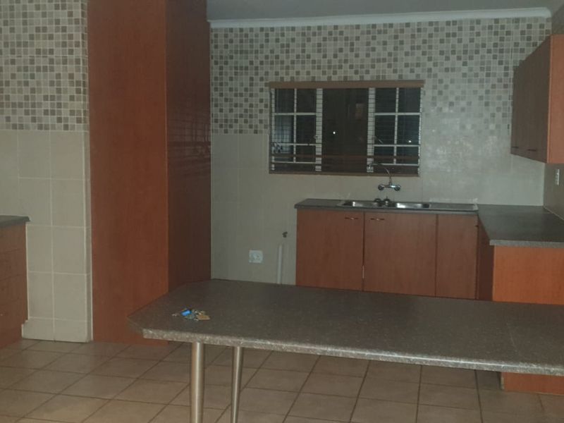 A functional kitchen featuring built-in wooden cabinetry, laminate countertops, a breakfast bar, and a tiled backsplash with an integrated oven and hob.