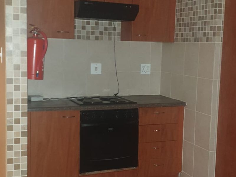 A compact kitchen featuring wooden cabinetry, a built-in oven, hob, extractor fan, and tiled backsplash, offering a functional layout for meal preparation.