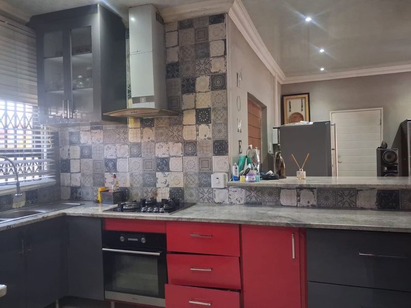 Kitchen featuring granite countertops, a gas hob with extractor fan, double sink, and a decorative tiled backsplash with a breakfast bar.