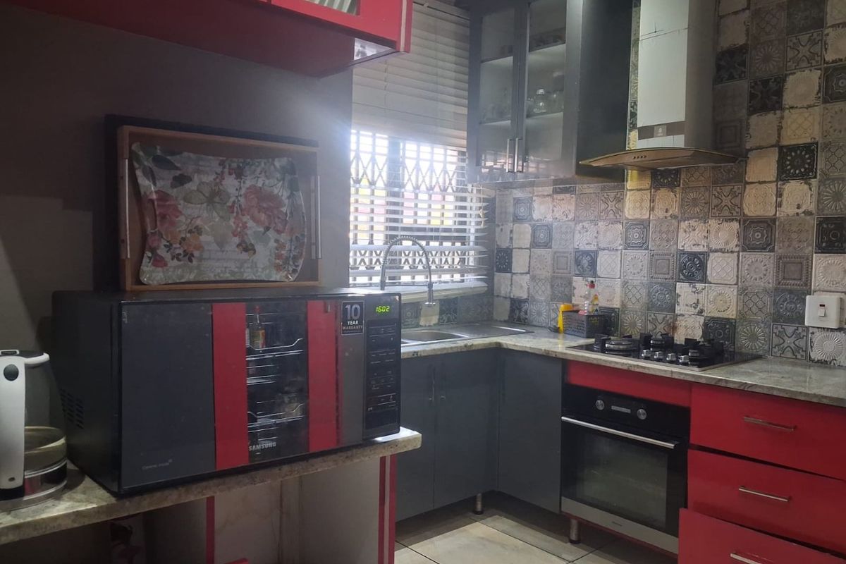 Compact kitchen featuring granite countertops, built-in oven, gas hob, extractor fan, and decorative tiled backsplash with ample storage cabinetry.