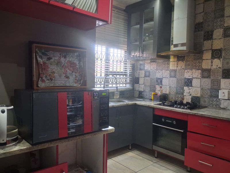 Compact kitchen featuring granite countertops, built-in oven, gas hob, extractor fan, and decorative tiled backsplash with ample storage cabinetry.