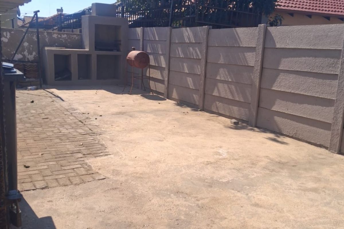 Rear outdoor area featuring a built-in braai, paved section, and precast concrete boundary wall, offering potential for landscaping or entertainment space development.