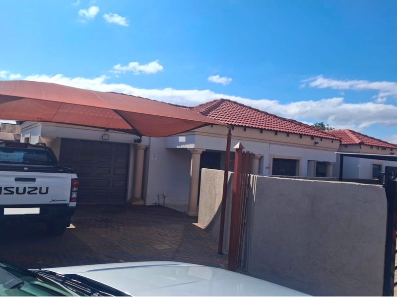Front exterior view of the house featuring a tiled roof, paved driveway, and a shade sail carport covering the garage entrance.