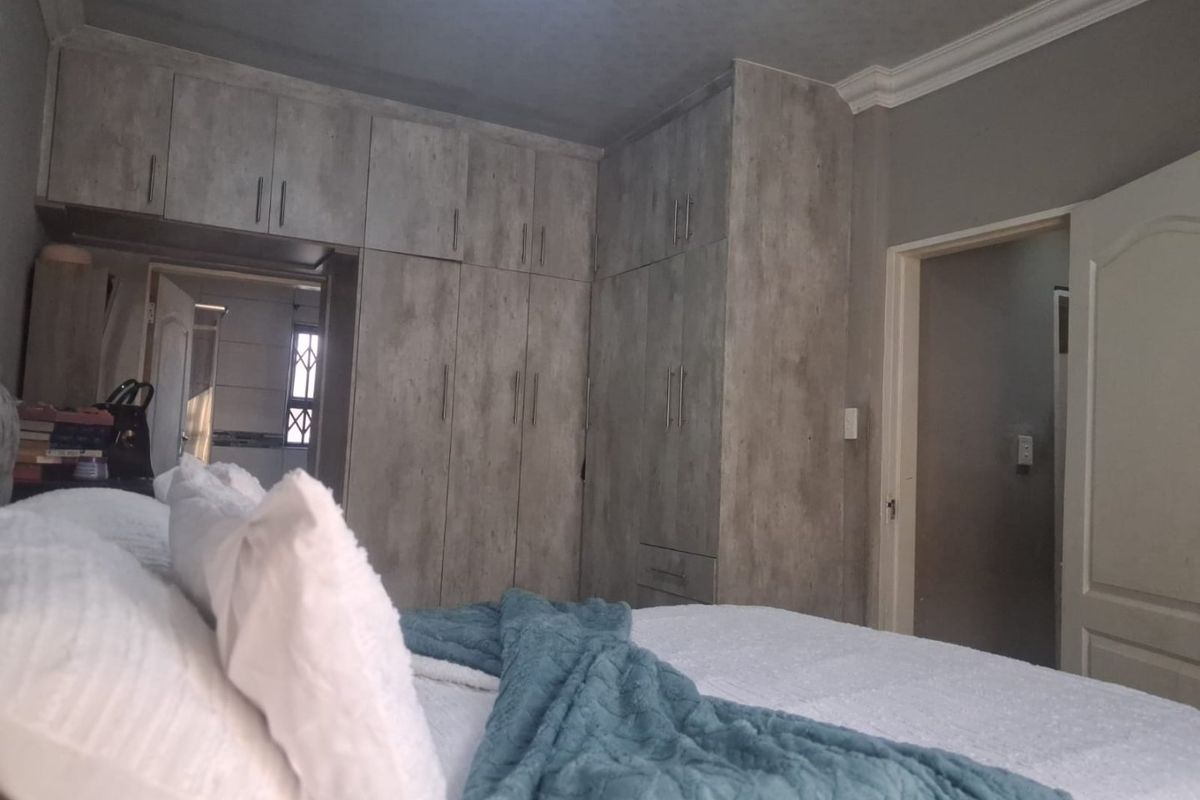 A well-maintained bedroom featuring extensive built-in cupboards with a modern wood-grain finish and decorative crown molding.